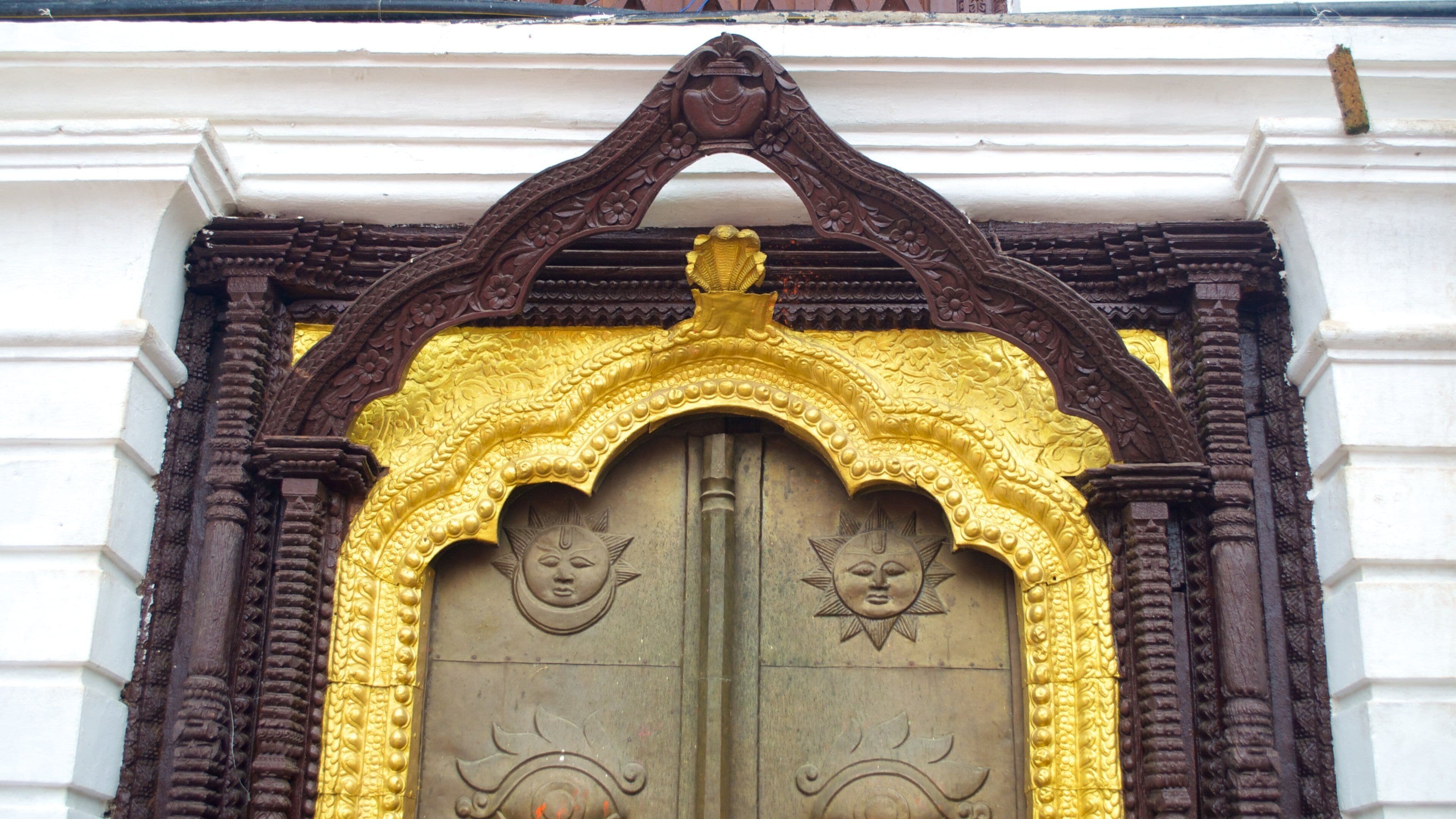 A detailed architectural entrance with ornate carvings and a golden arch.