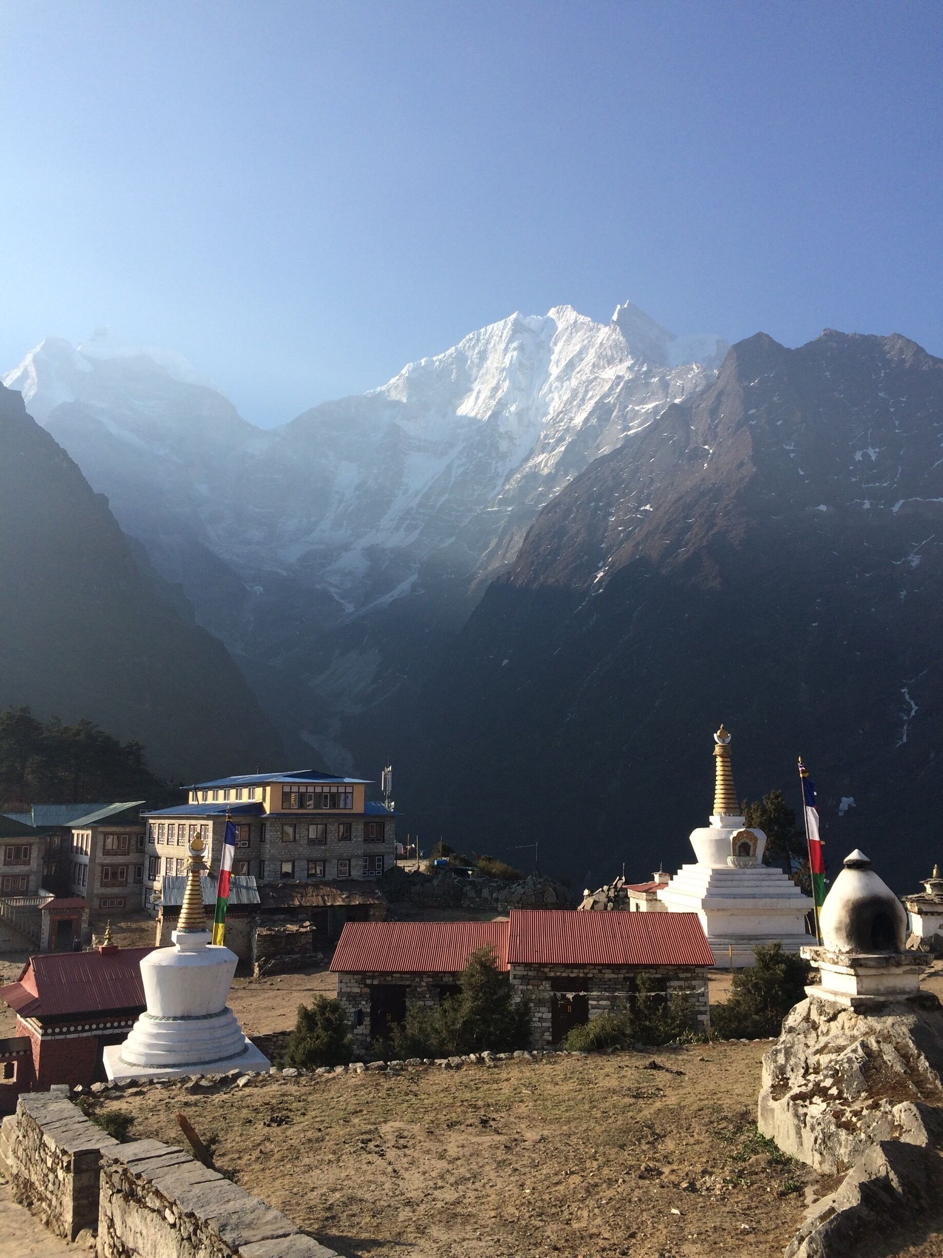 A mountainous landscape with snow-capped peaks, a monastery with prayer wheels, and a small settlement with buildings.