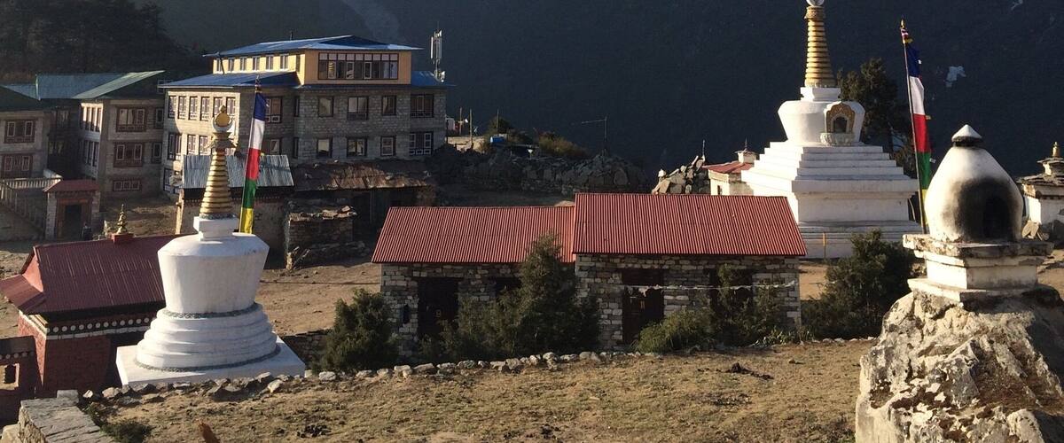 A mountainous landscape with snow-capped peaks, a monastery with prayer wheels, and a small settlement with buildings.