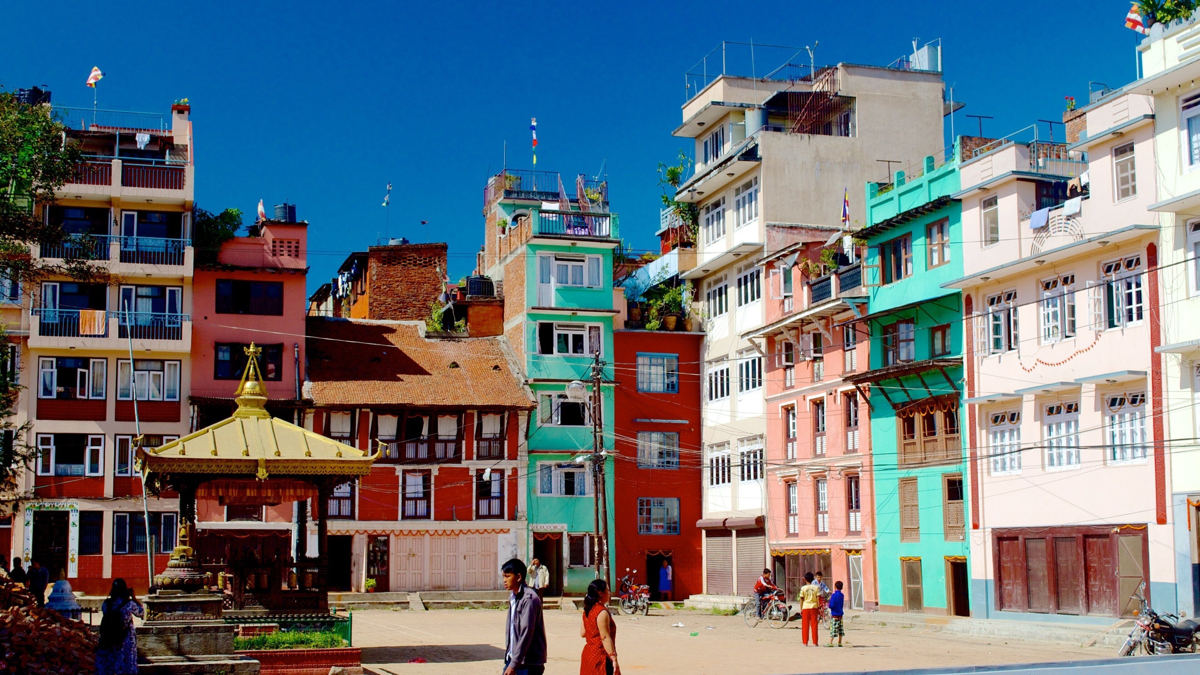 A colorful street with traditional buildings, a small shrine, and people walking.
