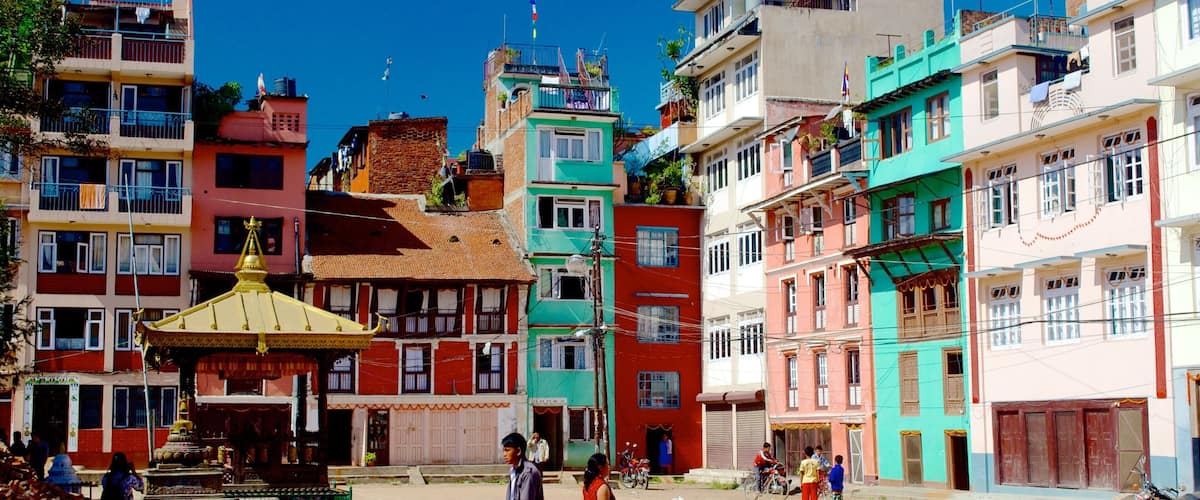 A colorful street with traditional buildings, a small shrine, and people walking.