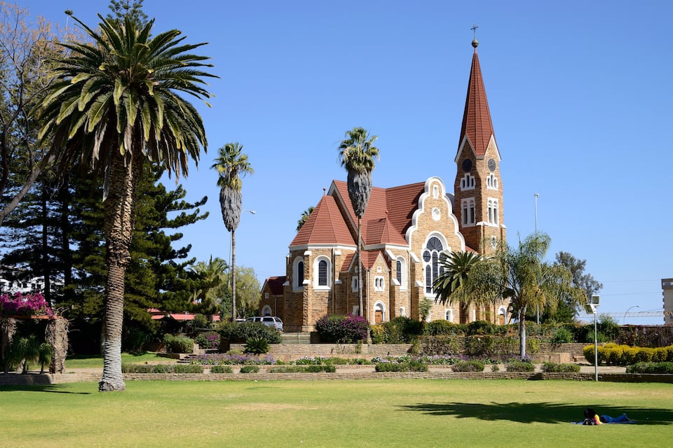 A church with a tall steeple and a clock tower, surrounded by palm trees and well-maintained gardens.