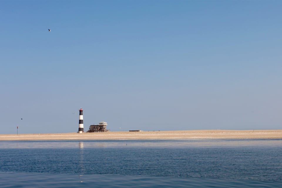 Un faro junto a un mar tranquilo y cielos despejados.