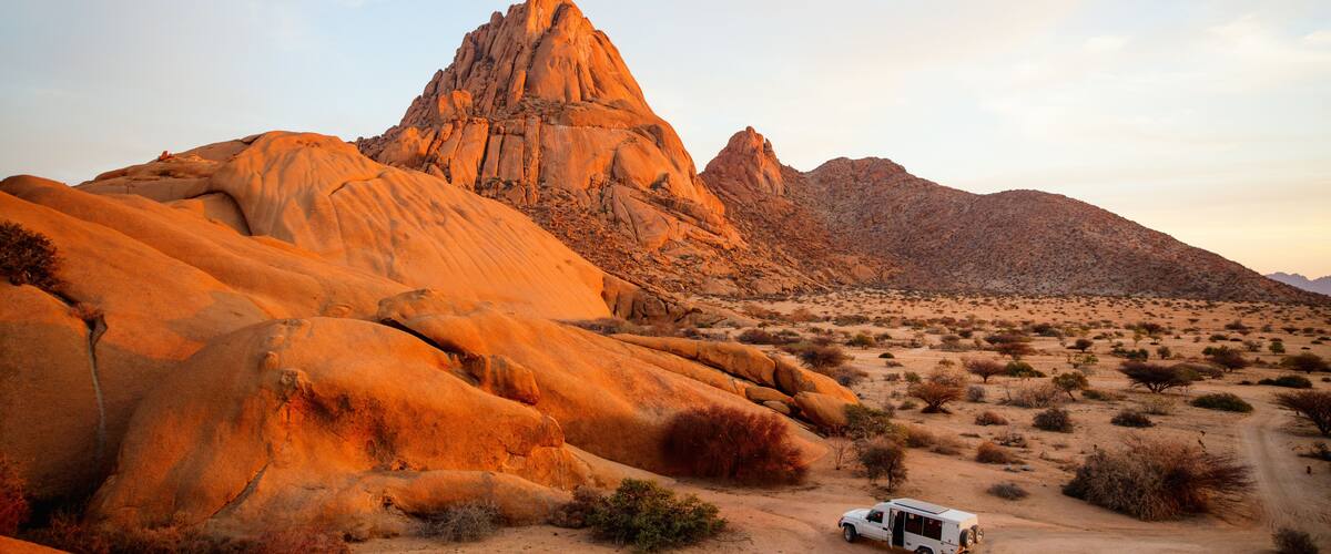 A desert landscape with a prominent rock formation and a white vehicle parked on the ground.