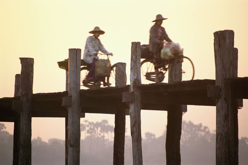 Two people riding bicycles on a wooden bridge during sunset.