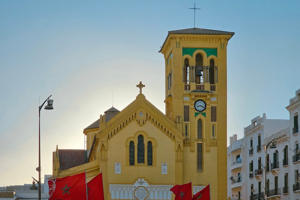 Eine gelbe Kirche mit einem Glockenturm, roten Flaggen und einem Kreuz auf dem Dach.