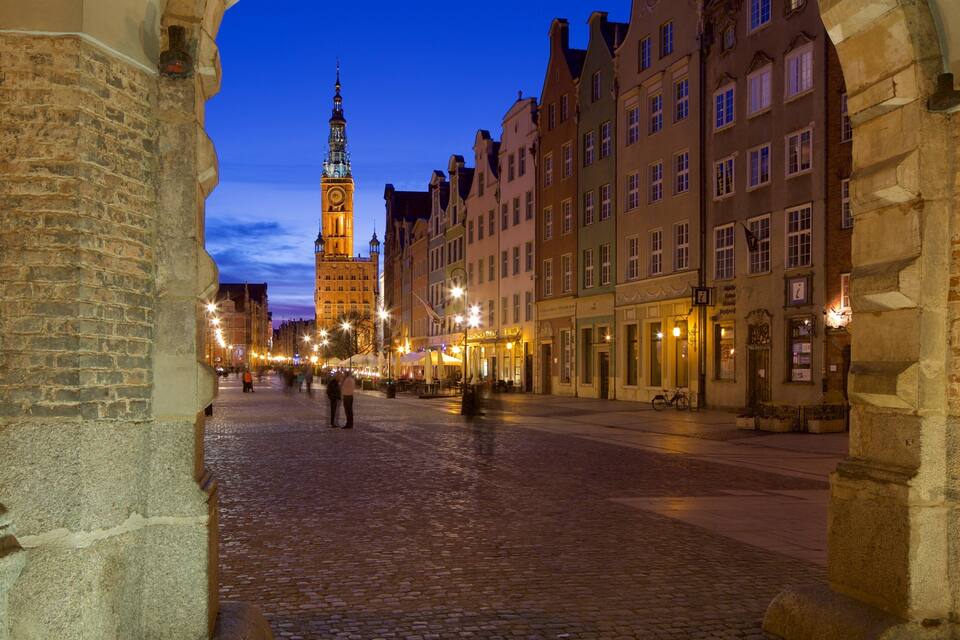 A cobblestone street with historic buildings and a clock tower at dusk.