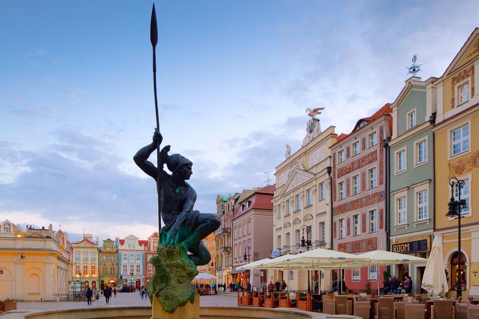 Estátua de um homem segurando uma lança em uma praça cercada por edifícios coloridos.