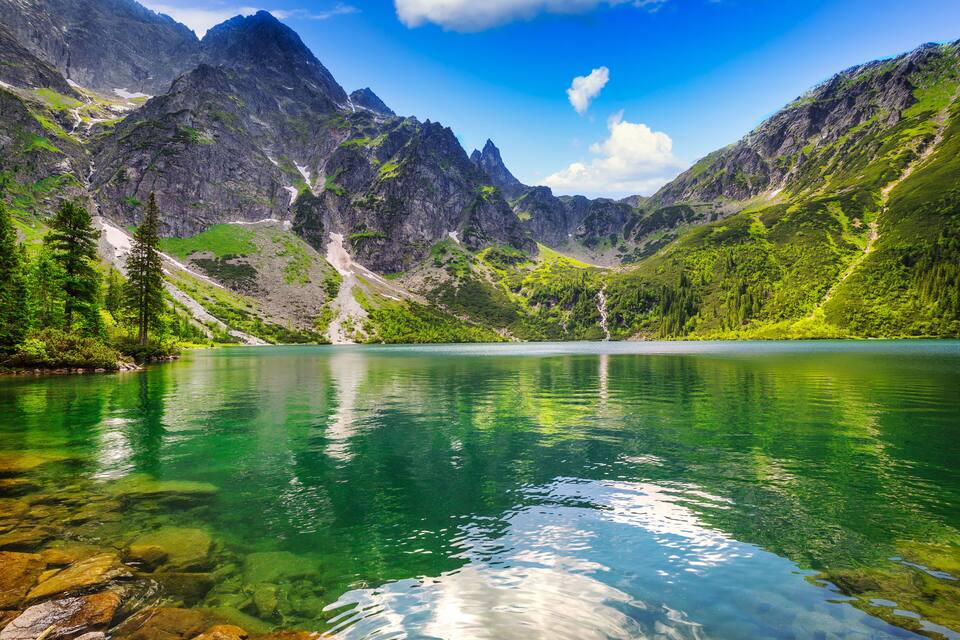 A mountain lake with clear water reflecting the surrounding peaks and greenery.