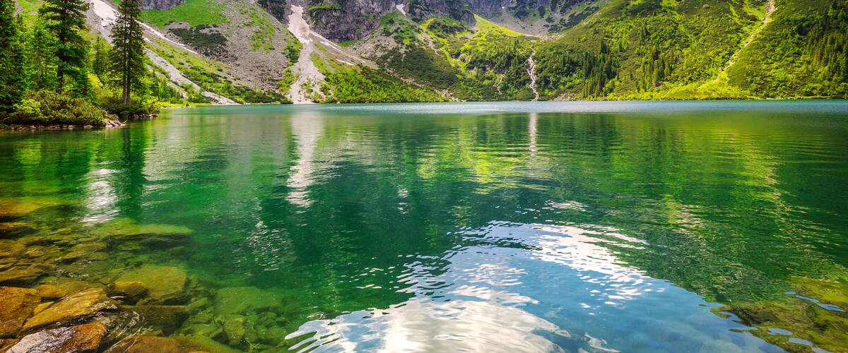 A mountain lake with clear water reflecting the surrounding peaks and greenery.