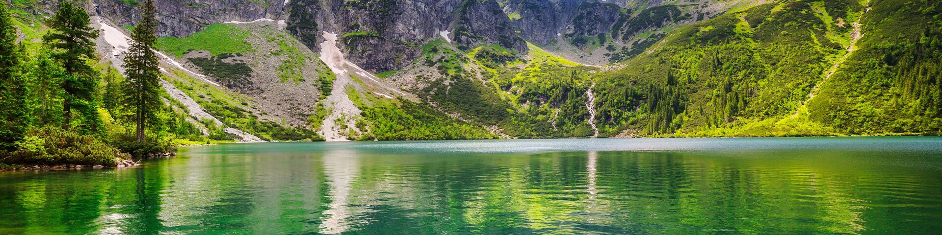 A mountain lake with clear water reflecting the surrounding peaks and greenery.
