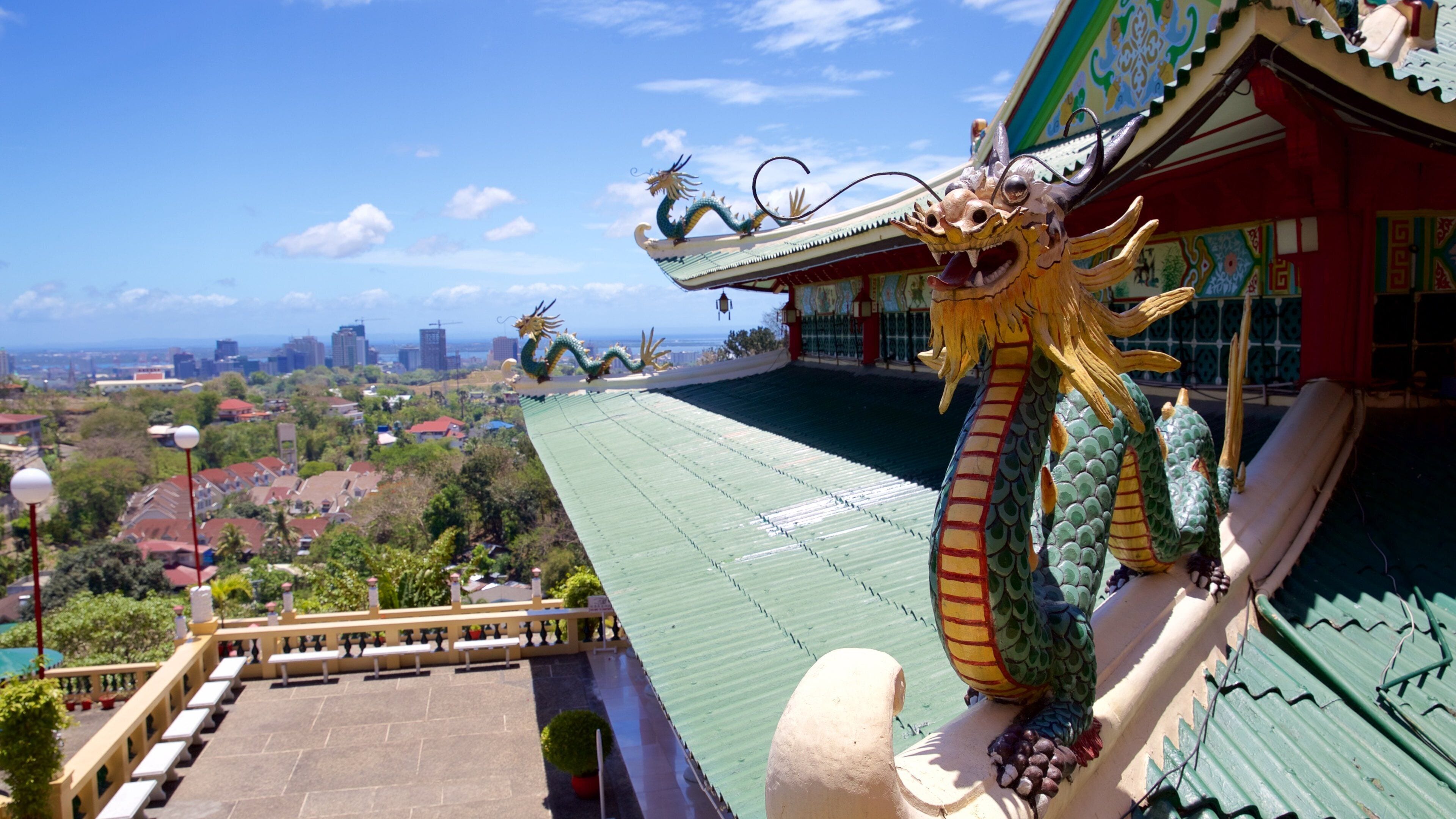 A dragon statue on a roof, a cityscape in the background, and a green roof.
