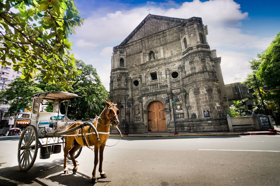 A horse-drawn carriage in front of a historic stone building with a large wooden door and arched windows.