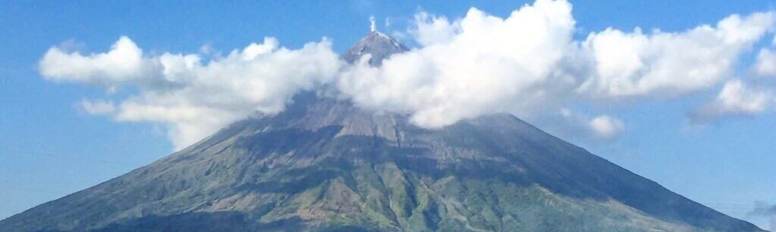 Un volcán con una capa de nubes, rodeado de campos de arroz y palmeras.