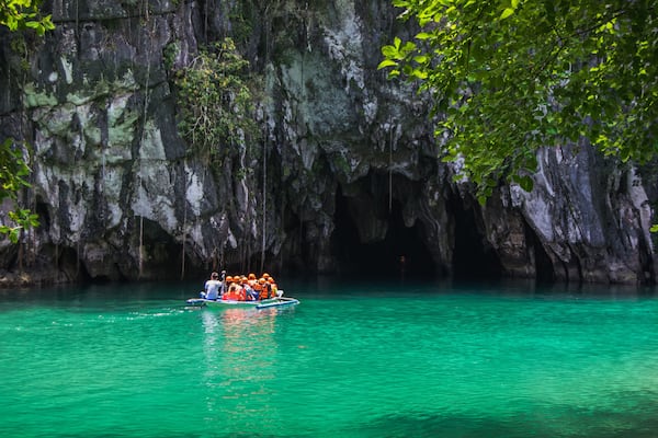 A group of people in a boat on turquoise water with a rocky cave wall in the background.