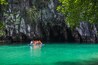 Um grupo de pessoas em um barco sobre águas turquesa, com uma parede rochosa de caverna ao fundo.