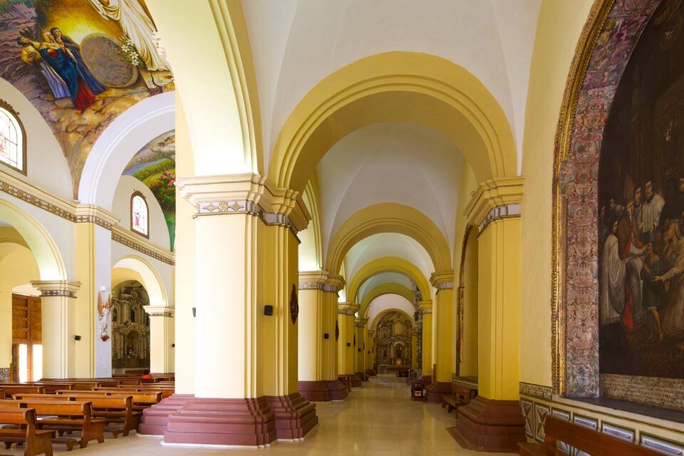 Interior d'una església amb sostres arquejats, pews de fusta i un mural gran a la pared.