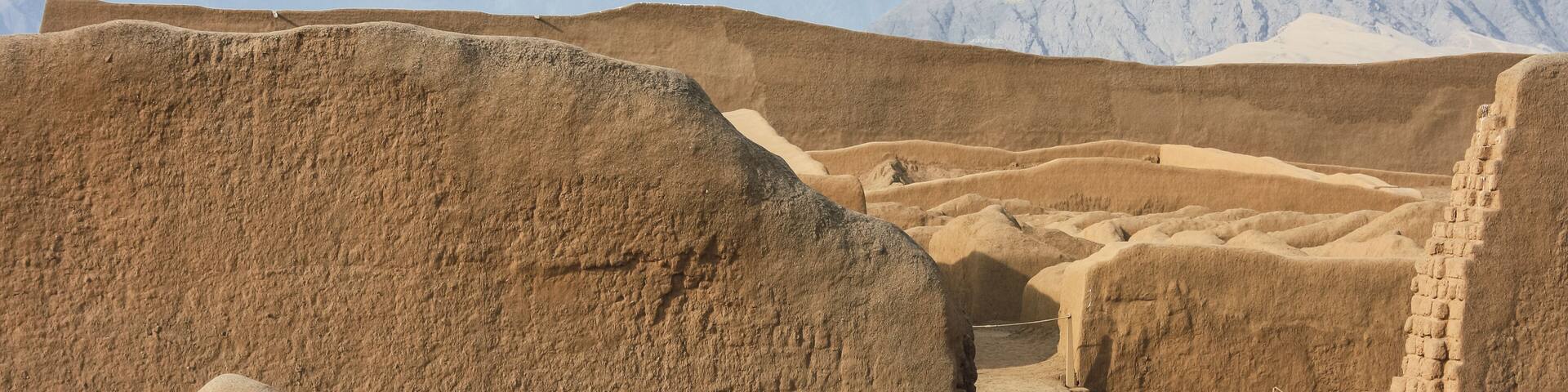 Ancient ruins with stepped structures and a mountainous backdrop.