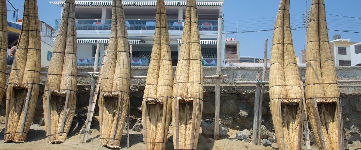 Bamboo structures in a sandy area with a building in the background.