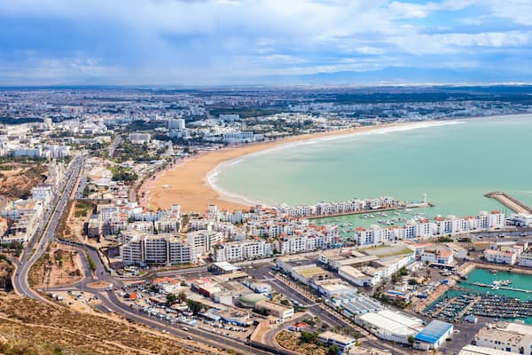Un paysage urbain côtier comprenant une plage, un port de plaisance et une zone urbaine densément construite.