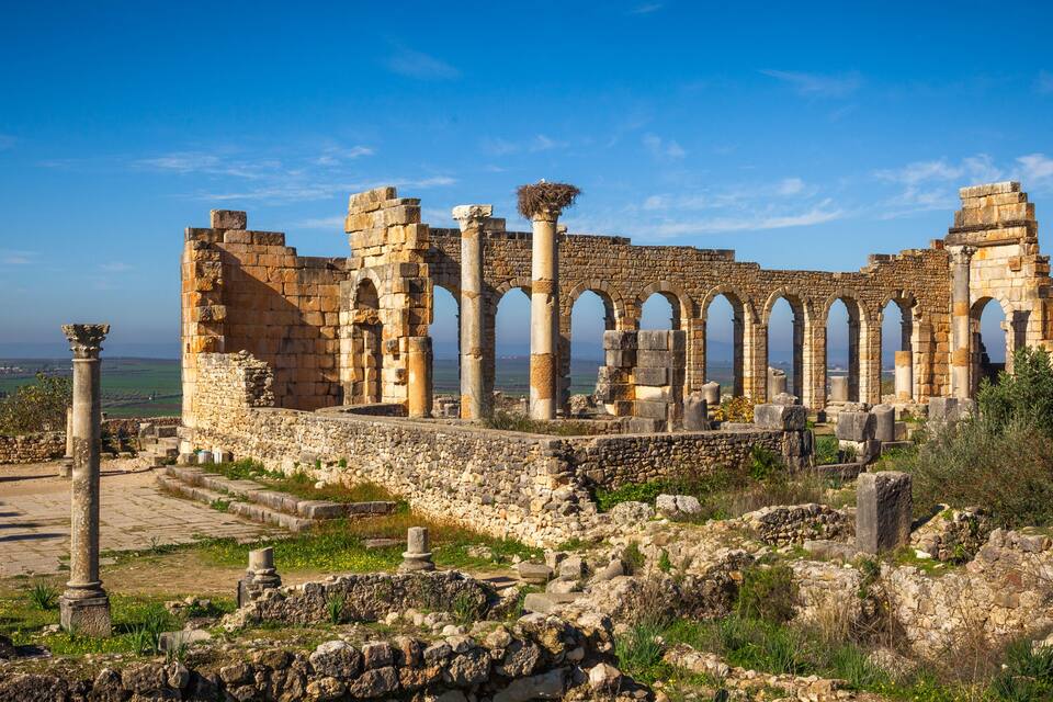 Ancient ruins with columns and arches, set against a clear blue sky.