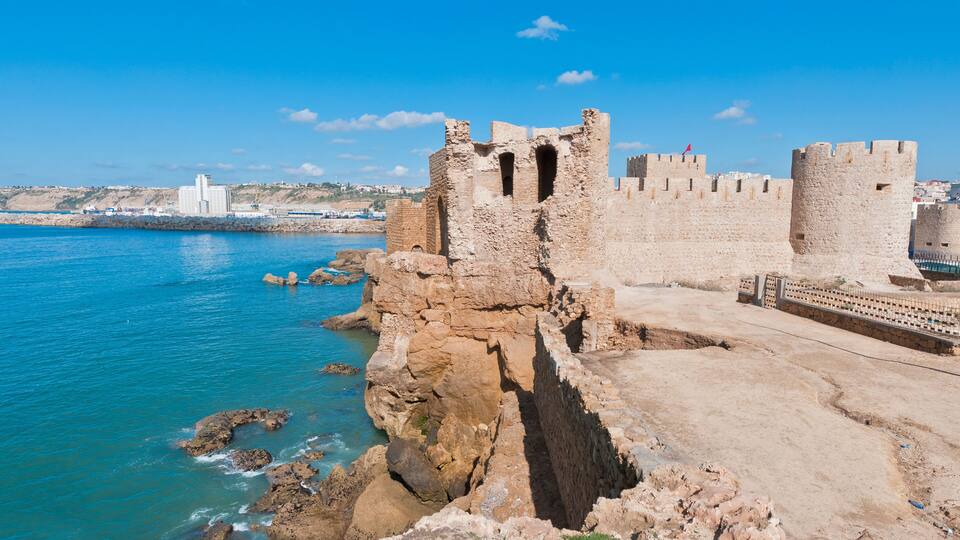 A coastal fortification with a clear view of the sea and a distant cityscape.
