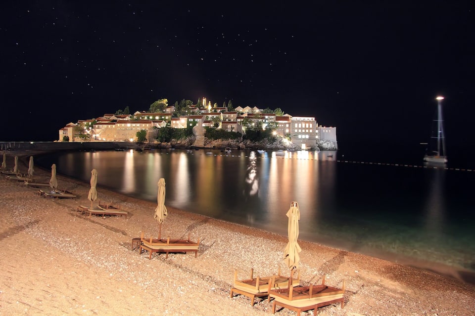Un poble costaner de nit amb edificis il·luminats i una mar tranquil·la.