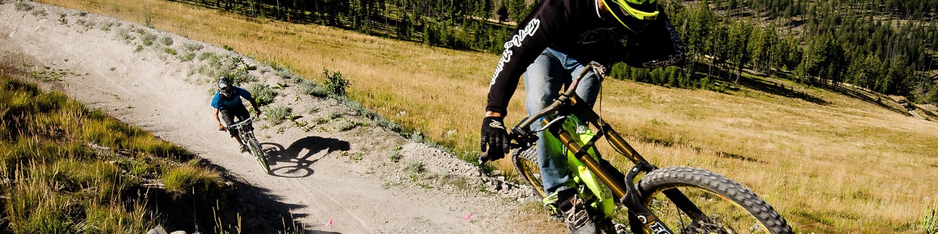 Un ciclista de montaña pedalea sobre un sendero de tierra, con una montaña boscosa al fondo.