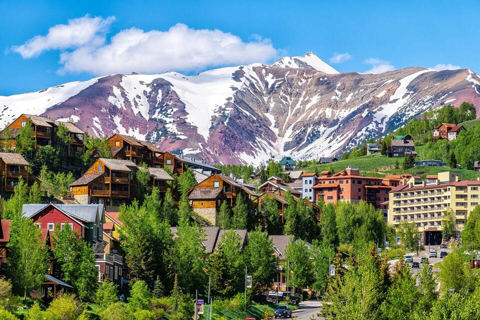 A mountain town with wooden houses, a road, and snow-capped peaks.