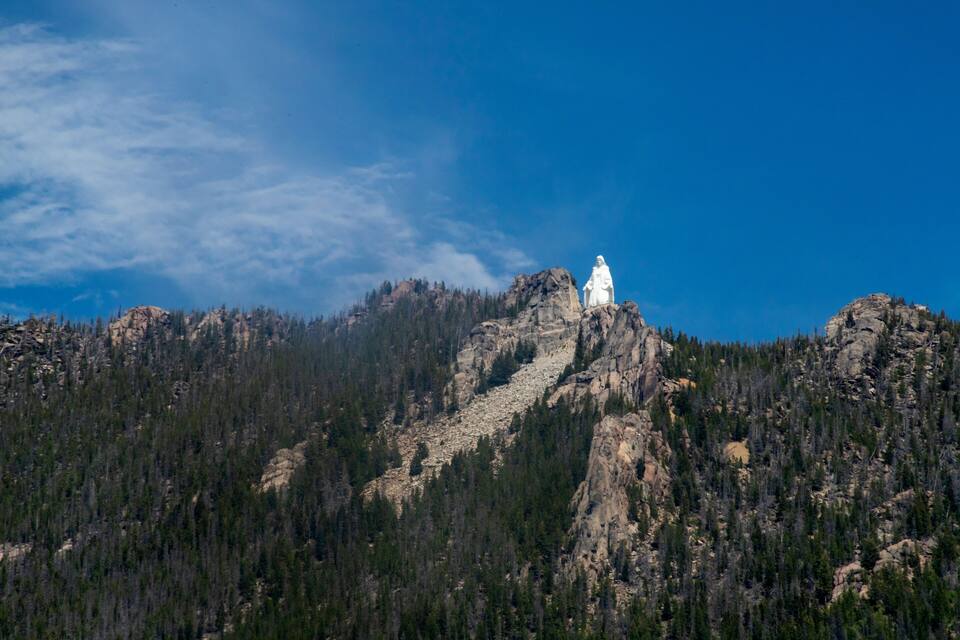A white statue on a mountain peak with dense forested slopes.