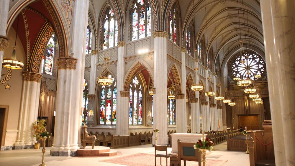 A grand cathedral interior with high vaulted ceilings, stained glass windows, and ornate chandeliers.