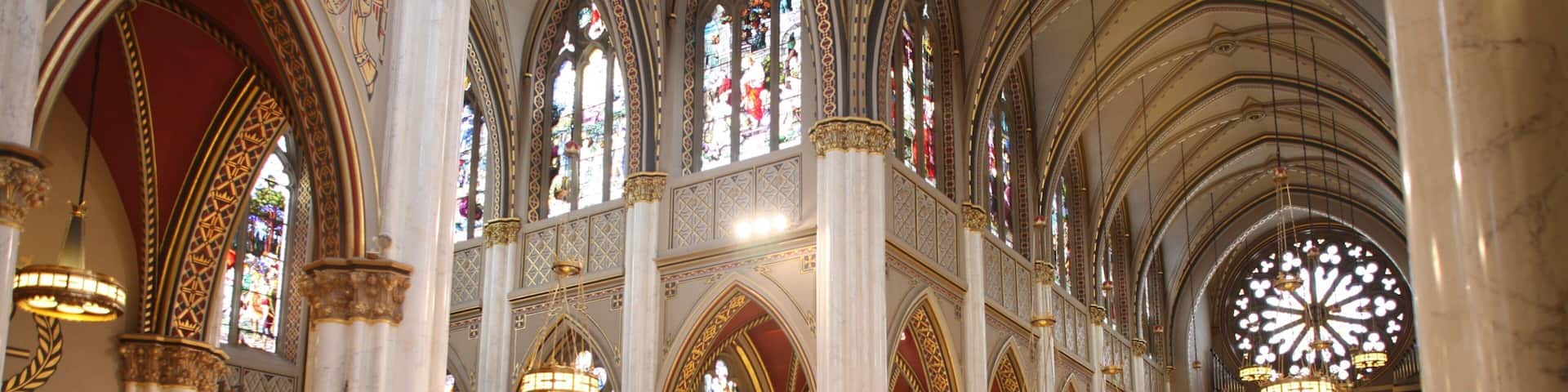 A grand cathedral interior with high vaulted ceilings, stained glass windows, and ornate chandeliers.