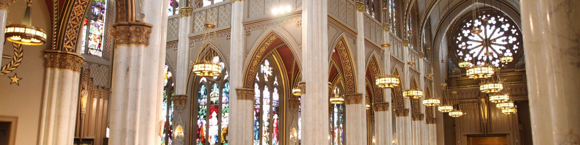 Interior imponente de una catedral con altos techos abovedados, vidrieras y candelabros ornamentados.