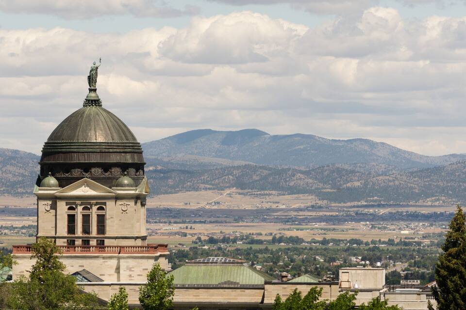 A historic building with a dome and statue, surrounded by mountains and a valley.
