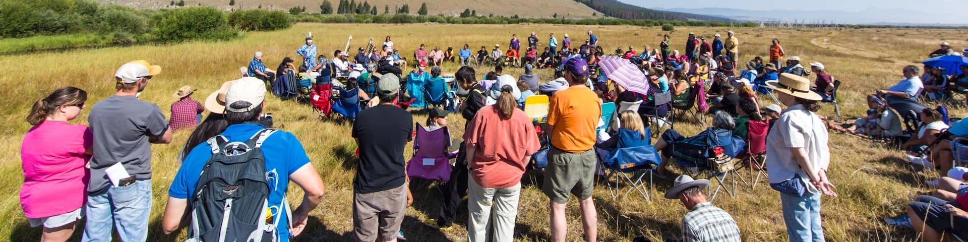 A large group of people gathered in an open field with a hilly landscape in the background.
