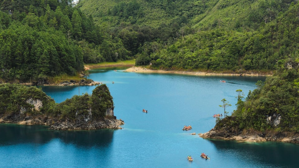 A calm lake surrounded by lush green hills, with several boats on the water.