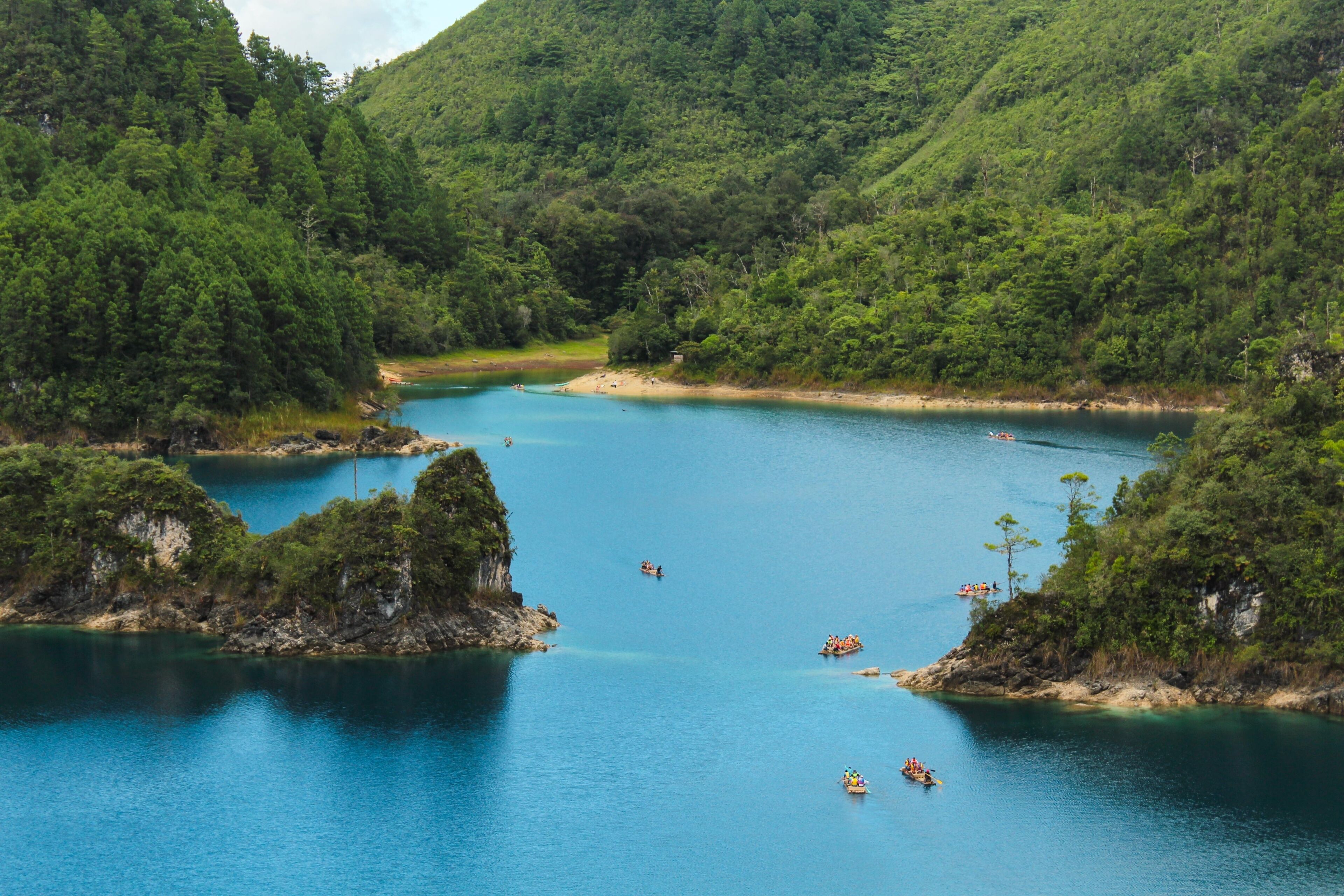 A calm lake surrounded by lush green hills, with several boats on the water.