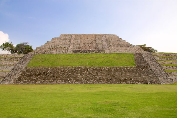 Une grande pyramide de pierre, à sommet plat et à base en gradins, entourée d’herbe verte et d’arbres.