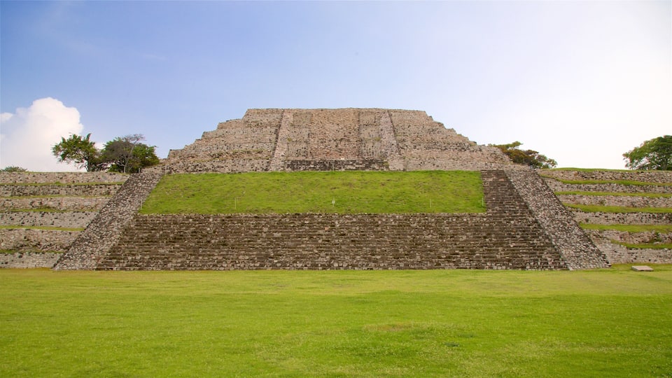 A large stone pyramid with a flat top and a stepped base, surrounded by green grass and trees.