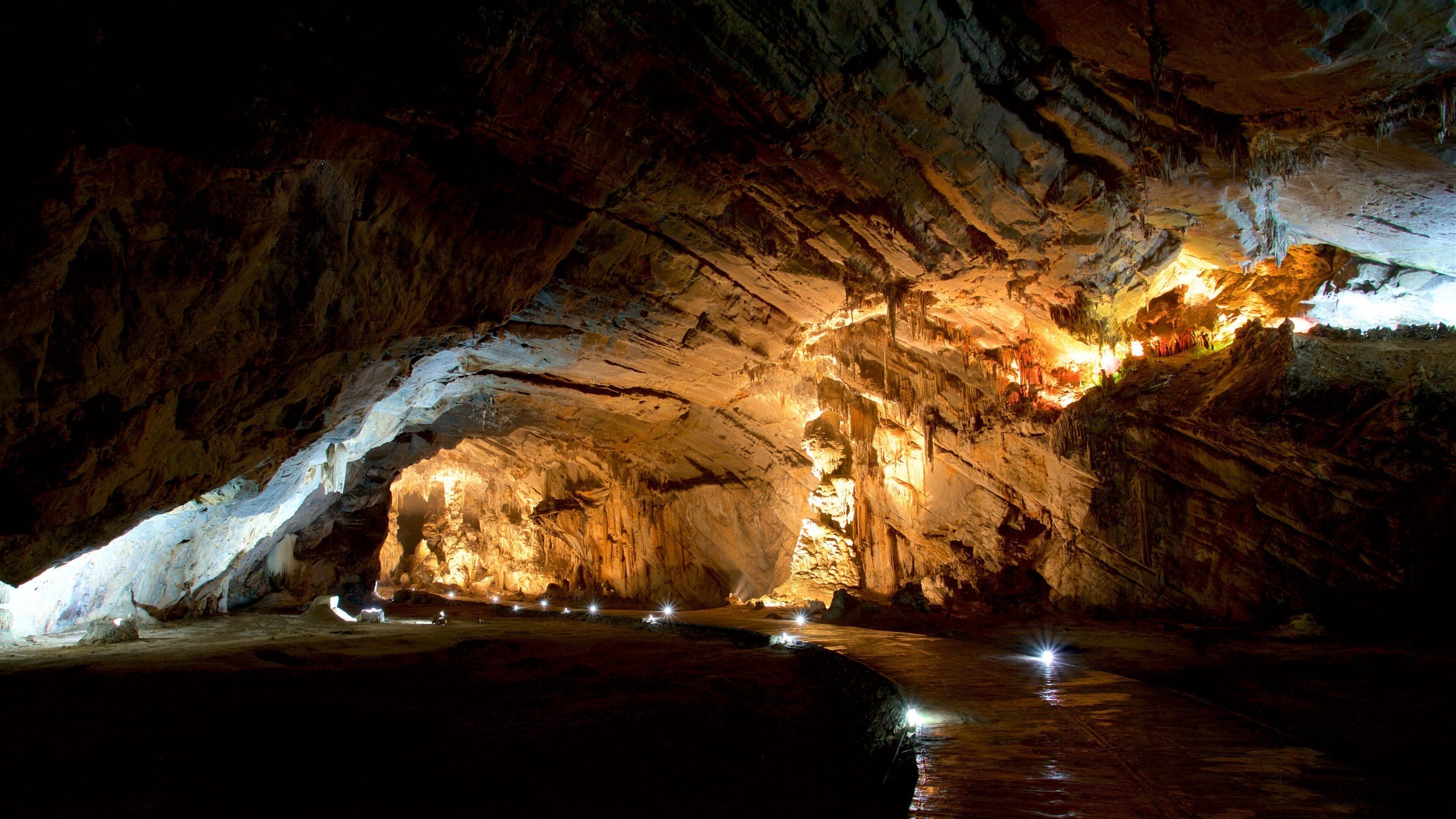 Una cueva con estalactitas iluminadas y un curso de agua.
