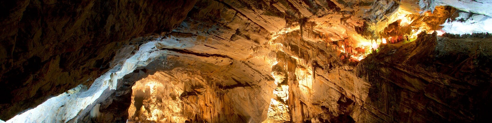 Una cueva con estalactitas iluminadas y un curso de agua.