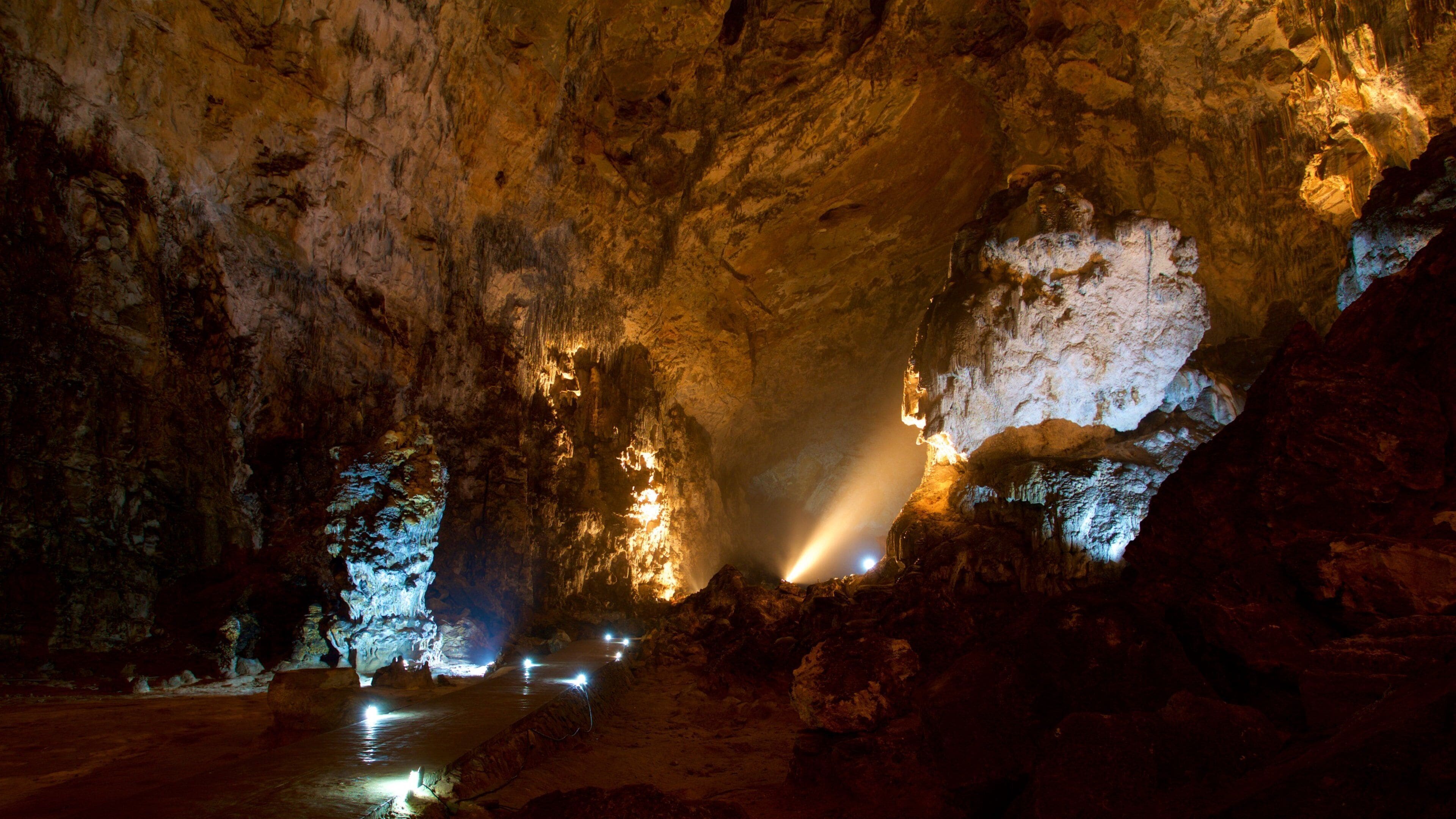 A cave with illuminated stalactites and a water stream.