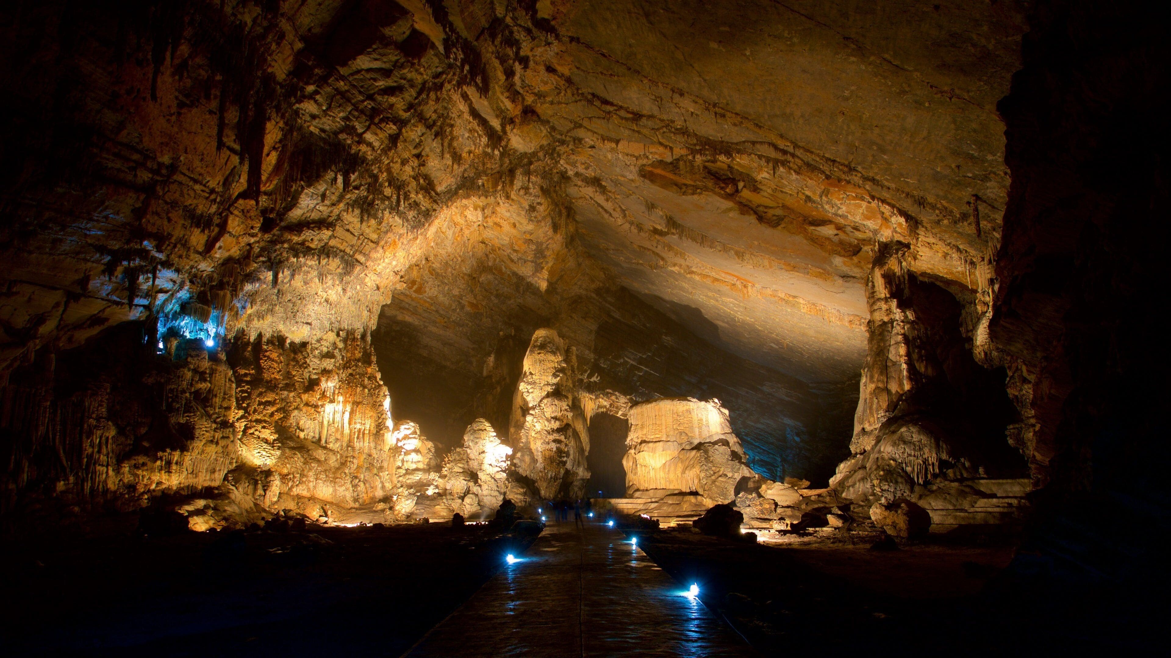 A cave with illuminated stalactites and a water channel.
