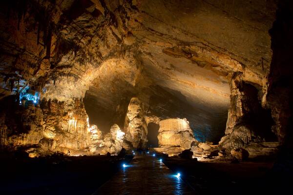 Eine Höhle mit beleuchteten Stalaktiten und einem Wasserlauf.