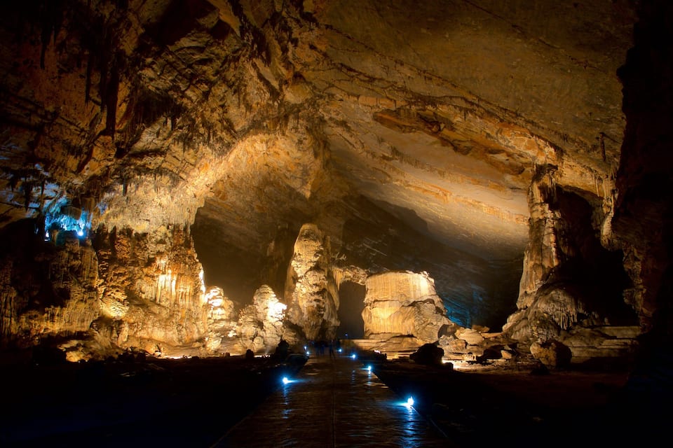 A cave with illuminated stalactites and a water channel.