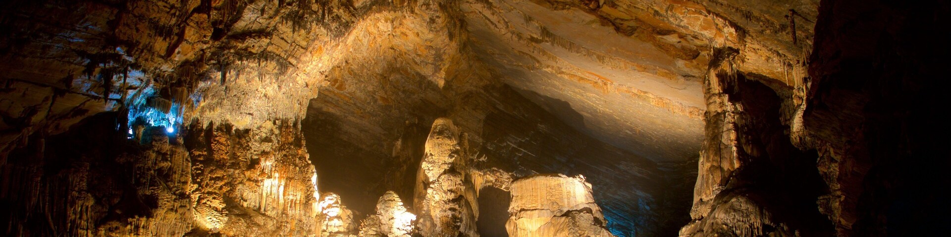Uma caverna com estalactites iluminadas e um canal de água.