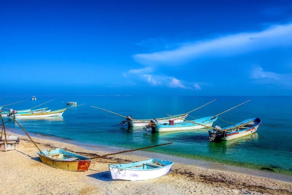 A beach with several small boats anchored in shallow water.
