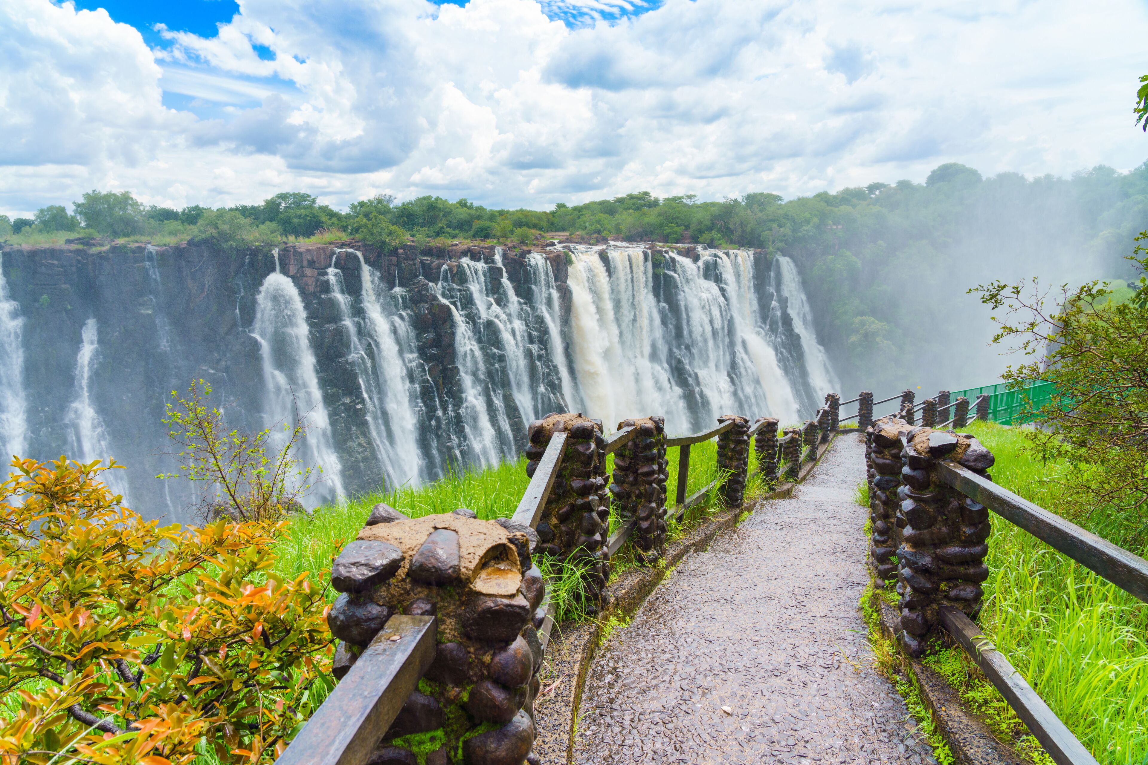 Walking way with view to the dramatic clouds and waterfall at Victoria Falls on the Zambezi River, Zimbabwe, Zambia.