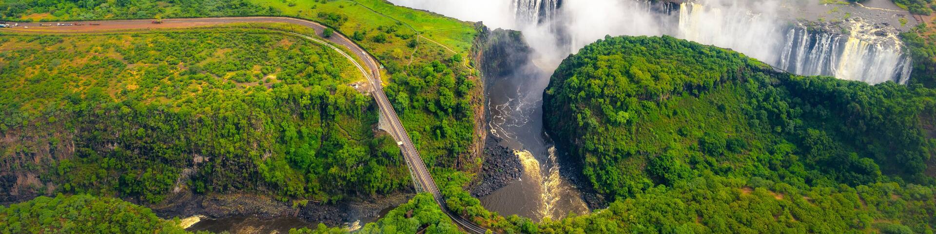 Victoria Falls in Zimbabwe and Zambia, Aerial helicopter photo, green forest around amazing majestic waterfalls of Africa. Livingston Bridge above the river