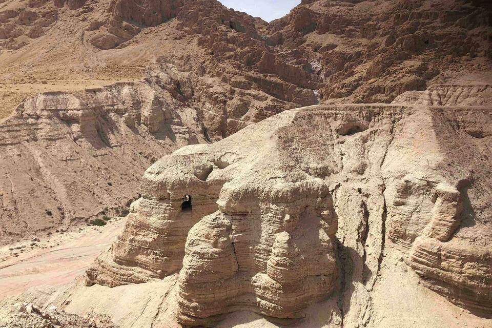 A rugged desert landscape with layered rock formations and a small cave entrance.